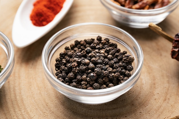 Black pepper in glass bowl on wood with other spices