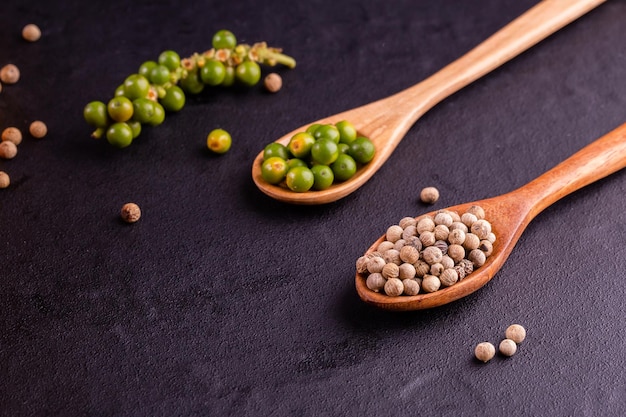 Black pepper spice peppercorn on wooden spoon and dark rustic background