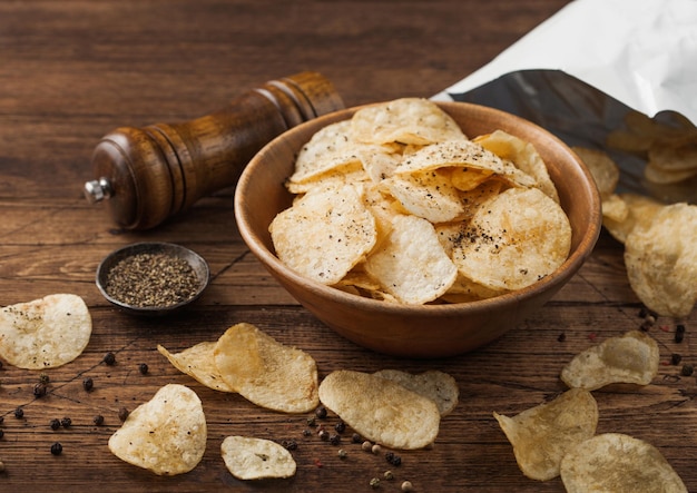 Black pepper taste potato crisps chips in wooden bowl bucket on wooden table background with mill and ground pepper with package