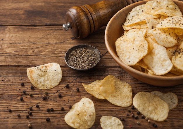 Black pepper taste potato crisps chips in wooden bowl bucket on wooden table background with mill and ground pepper