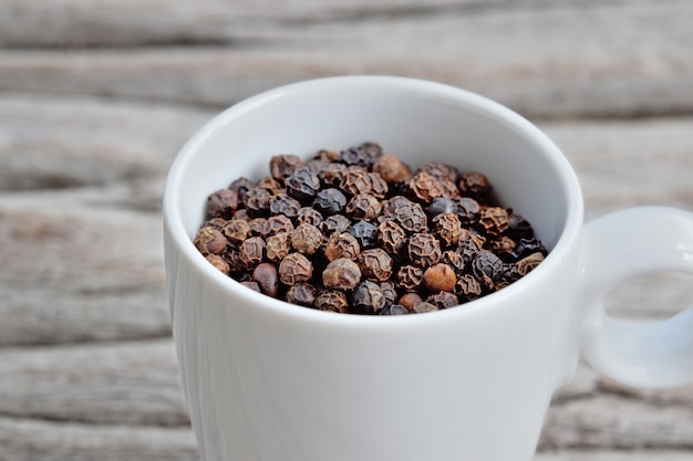 Black peppers in white cup on wooden