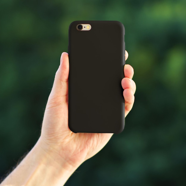 Black phone case mock up on a green blurred background in a man39s hand