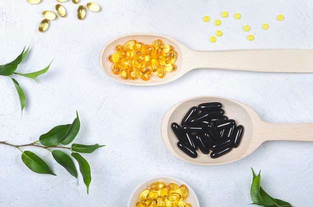 Black pill, yellow pill and wooden spoon on light background