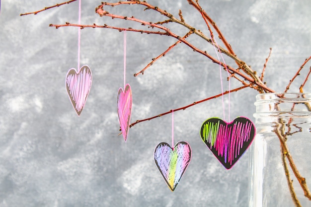 Black-pink hearts hang on branches on a gray concrete background. The concept of Valentine's Day.