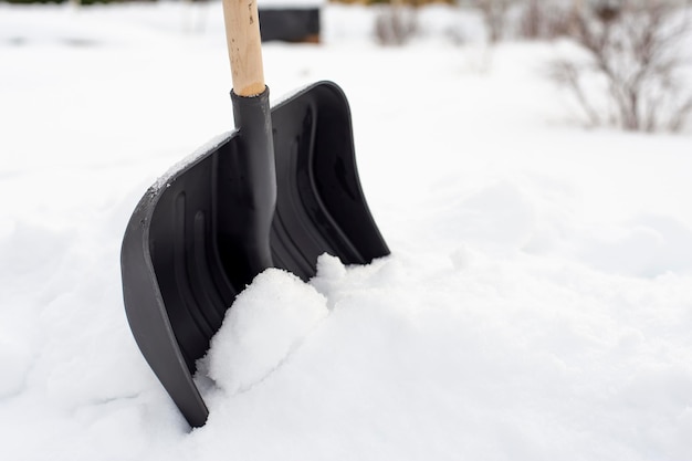 Black plastic shovel with a wooden handle standing in a snowdrift