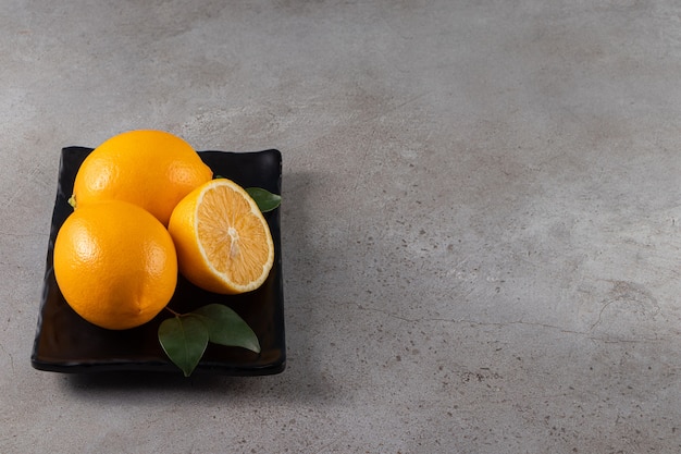 Black plate of fresh juicy lemons on stone background.