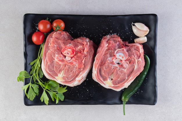 Black plate of raw lamb meat placed on stone table.