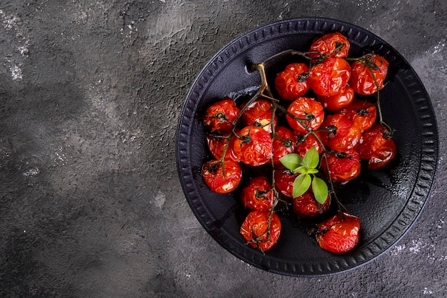 Photo black plate with confit tomatoes on dark surface.