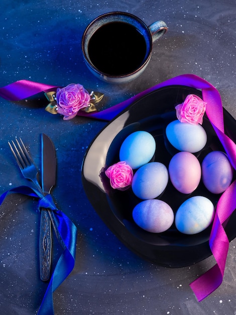 Black plate with Easter colored eggs on a stone dark table neon style colored light espresso cup