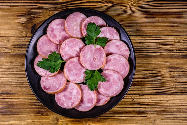 Black plate with sliced sausage on a wooden table Top view