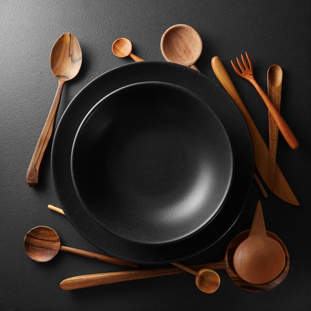 black plates and wooden spoon, fork, knife on a black table.