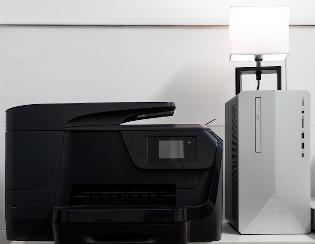 Black printer next to a grey and black pc with a lamp on