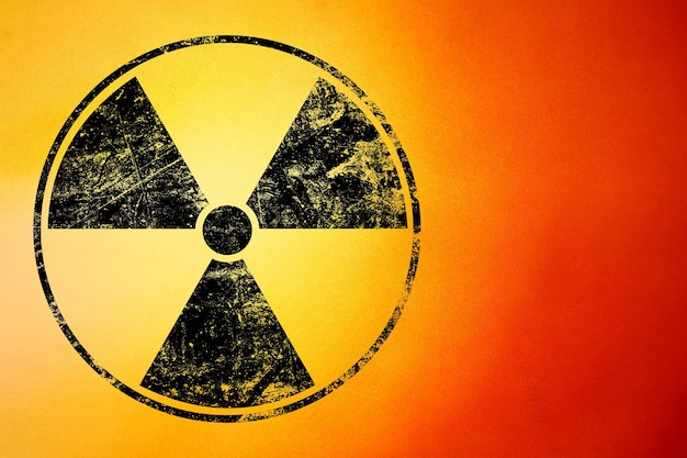 Black radioactive hazard warning sign painted over grunge yellow and red background with copy space