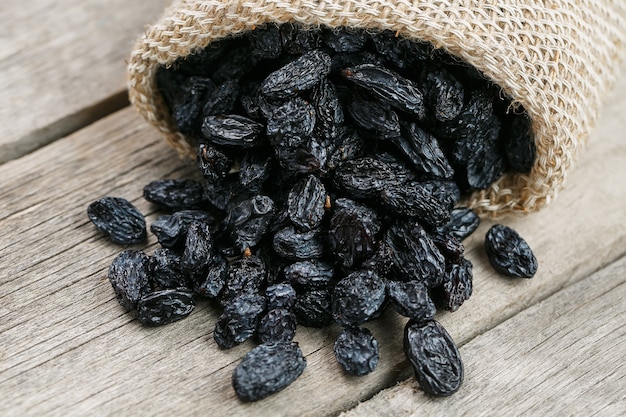 Black raisins in burlap bag over wooden gray table