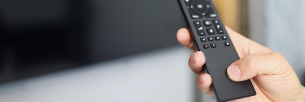 Black remote control in hand in front of tv remote control technology concept