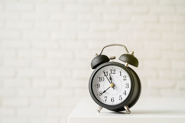 Black retro alarm clock on white brick wall background with copy space