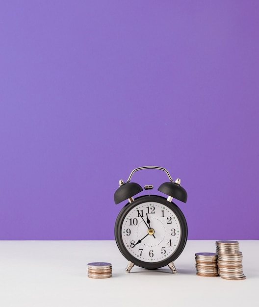 Black retro alarm clock with coins on purple background