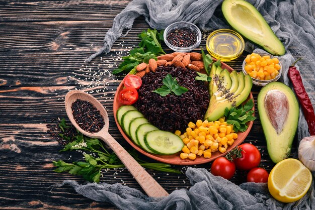 Black rice avocado cucumber corn and almonds On a wooden background Top view Free space for your text