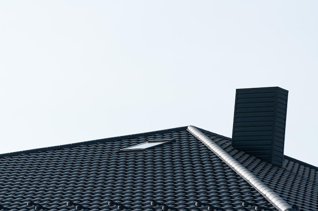 Black roof of a new house Roof covering with steel tiles Black roof with a skylight and a chimney