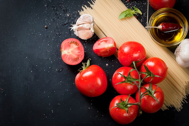 Black rustic tabletop with branch of tomatoes and herbs, top view