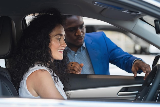 Black salesman describes car characteristics to lady client