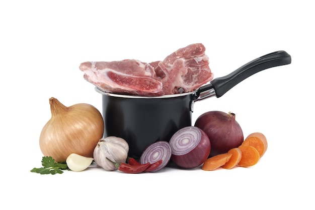 Black saucepan with pieces of raw pork inside and sliced vegetables isolated on white background