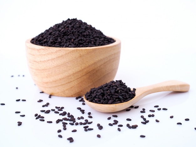 Black sesame seeds in wooden spoon isolated on white surface.