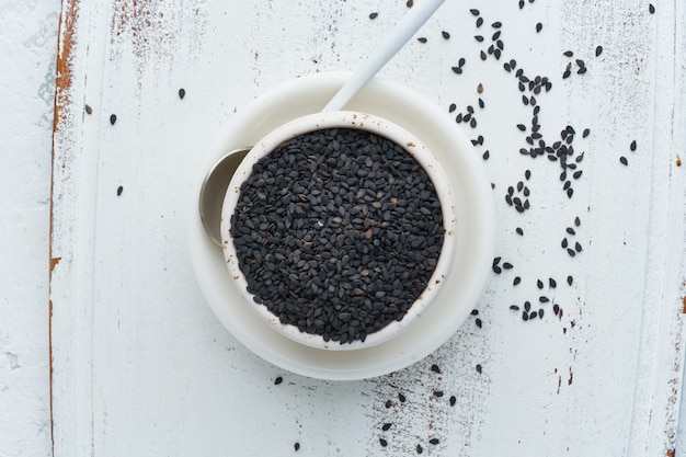 Black Sesame on white bowl with spoon. White wooden . Top view,