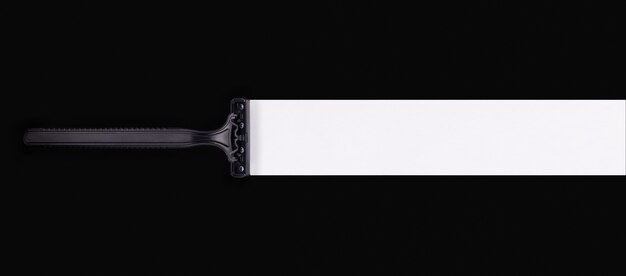 Black shaving razor on black background with a white trace after itself. Empty place for text on right.