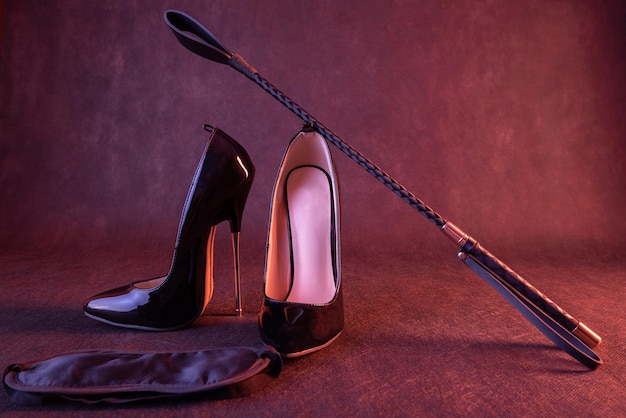 Black shiny high heel shoes and a whip on a dark background