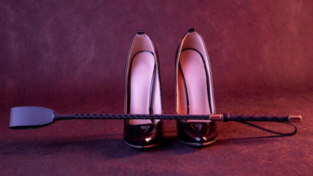 Black shiny high heel shoes and a whip on a dark background