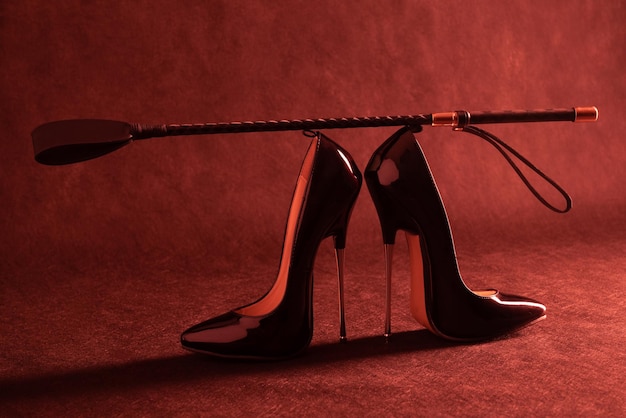 Black shiny high heel shoes and a whip on a dark background