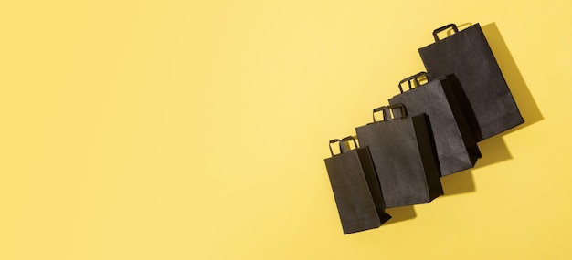 Black shopping bags on black friday sale yellow background with copy space in banner format