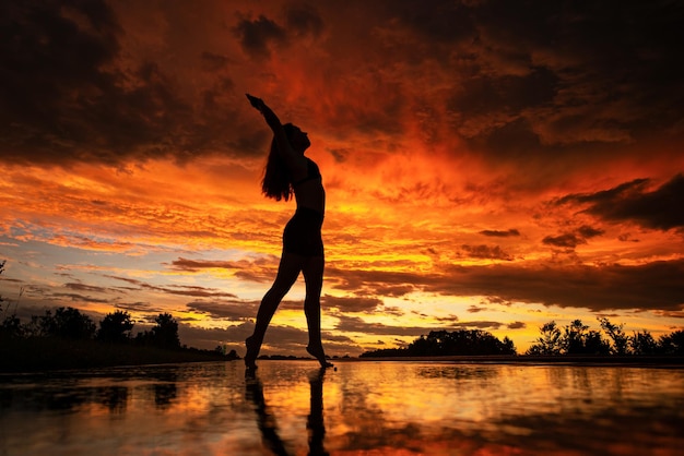 Black silhouette of pretty girl or beautiful woman sexy slim model with long hair poses on sea beach