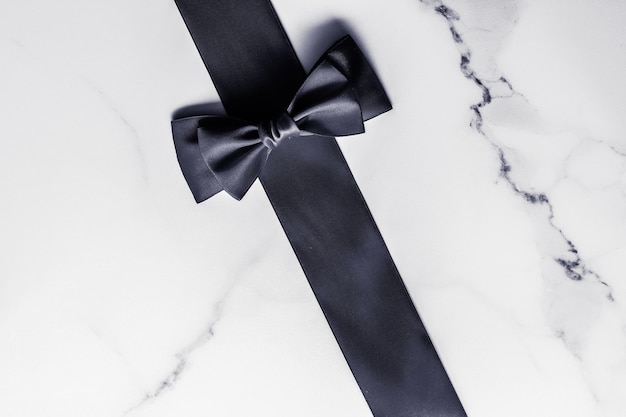 Black silk ribbon and bow on marble background flatlay