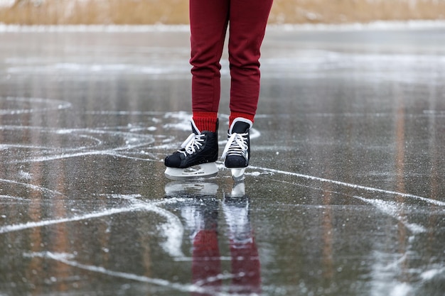 Black skates on ice Women's legs in burgundy pants stand on the surface of a frozen forest lake