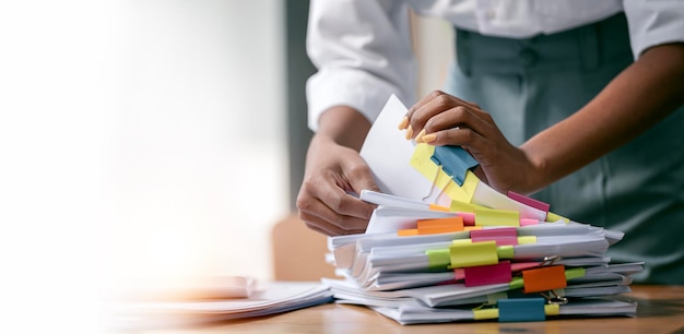 Black skin woman hands working in Stacks of paper files for searching and checking unfinished document achieves on folders papers