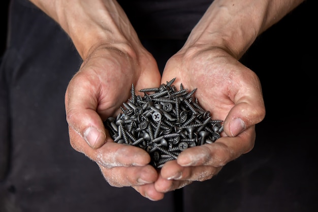 Black small self tapping screws for steel profile of drywall on young adult man hand on light gray table. Opened palm. Closeup.