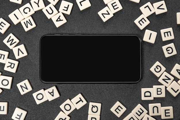 Black smartphone with blank screen in frame made of white letters of English alphabet on gray background Copy space