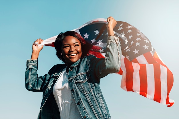 Black smiling female raising hands with USA flag