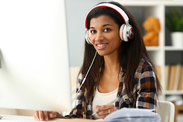 Black smiling woman sitting at workplace wearing headphones