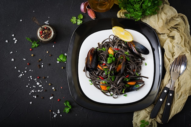 Black spaghetti. Black seafood pasta with mussels over black table. Mediterranean delicacy food. Flat lay. Top view