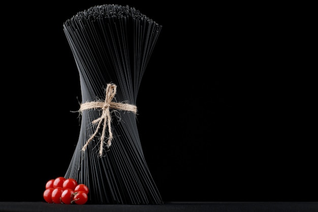 Black spaghetti pasta is raw on a black with fresh tomatoes