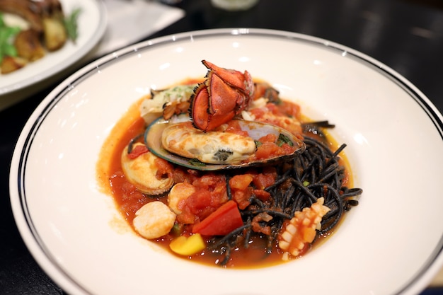 Black Spaghetti Stir fry with seafood such as lobster, mussels, squid, scallops in a white dish in the restaurant Black comes from the ink of squid. 