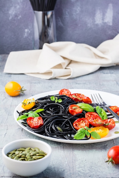 Black spaghetti with cuttlefish ink, with dried tomatoes, pumpkin seeds and sesame seeds on a plate on the table. Gourmet food. Vertical view