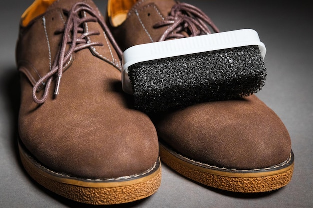 A black sponge for cleaning shoes lies on men's classic brown shoes with laces Suede shoe care concept