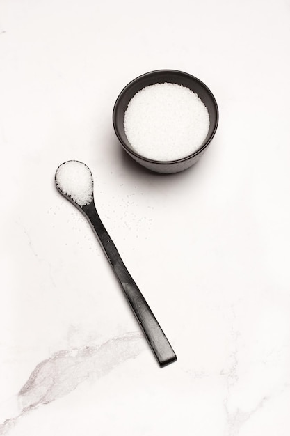 Black spoon and a black bowl with salt on a gray marble kitchen counter background with copy space