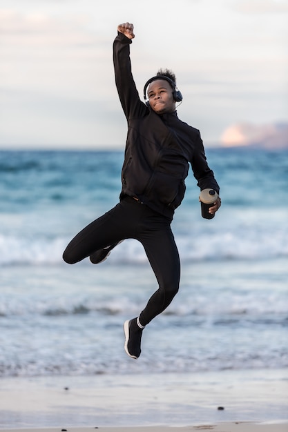 Black sportsman with cup jumping near sea