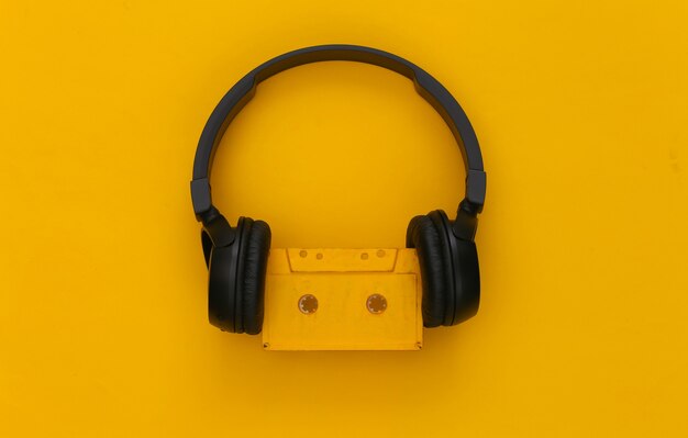 Black stereo headphones with a retro audio cassette on a yellow