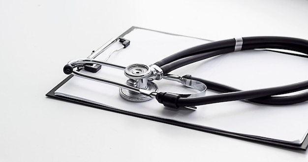 a black stethoscope sits on top of medical forms inserted into a clipon tablet On a white background